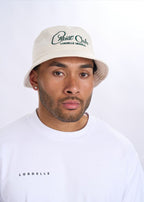 Man wearing a beige bucket hat and white shirt with text on a plain background