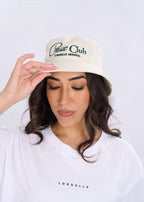 Woman wearing a white cap with text and a white shirt with text, on a light gray background
