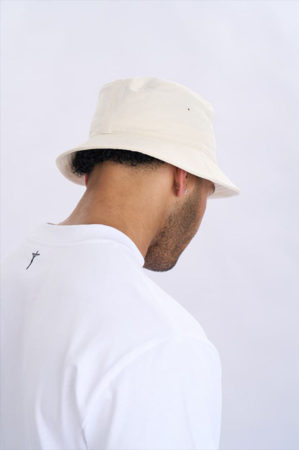 Person wearing a beige bucket hat and white shirt on a light grey background