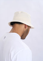 Person wearing a beige bucket hat and white shirt on a light grey background