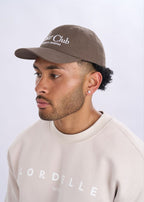 Man wearing a brown cap and beige sweatshirt with 'Lordelle' branding on a light grey background