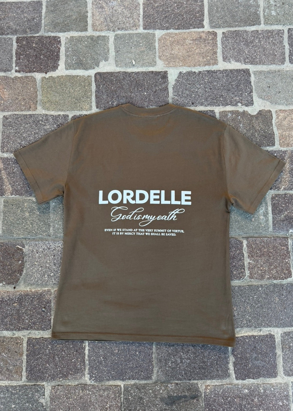 Brown t-shirt with 'LORDELLE God is my oath' text on a stone pavement background