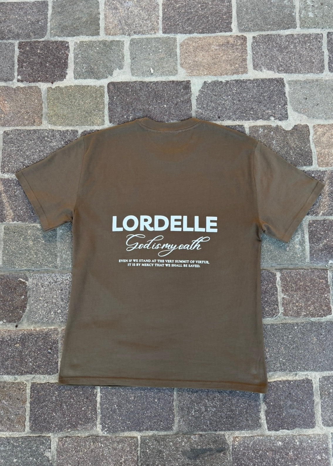 Brown t-shirt with 'LORDELLE God is my oath' text on a stone pavement background