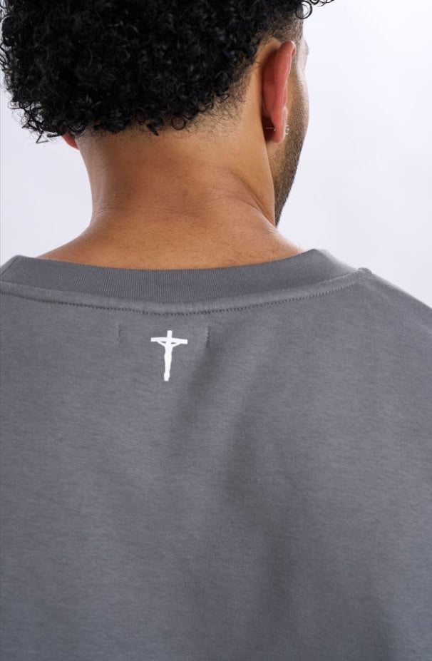 Grey t-shirt with a small logo on the back, worn by a person.