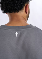 Grey t-shirt with a small logo on the back, worn by a person.
