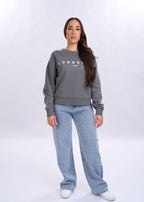 Woman wearing a grey sweatshirt with 'LORDEN' branding and blue jeans on a white background